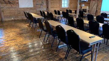 A conference room with long tables and chairs, wooden walls, and a projector screen.