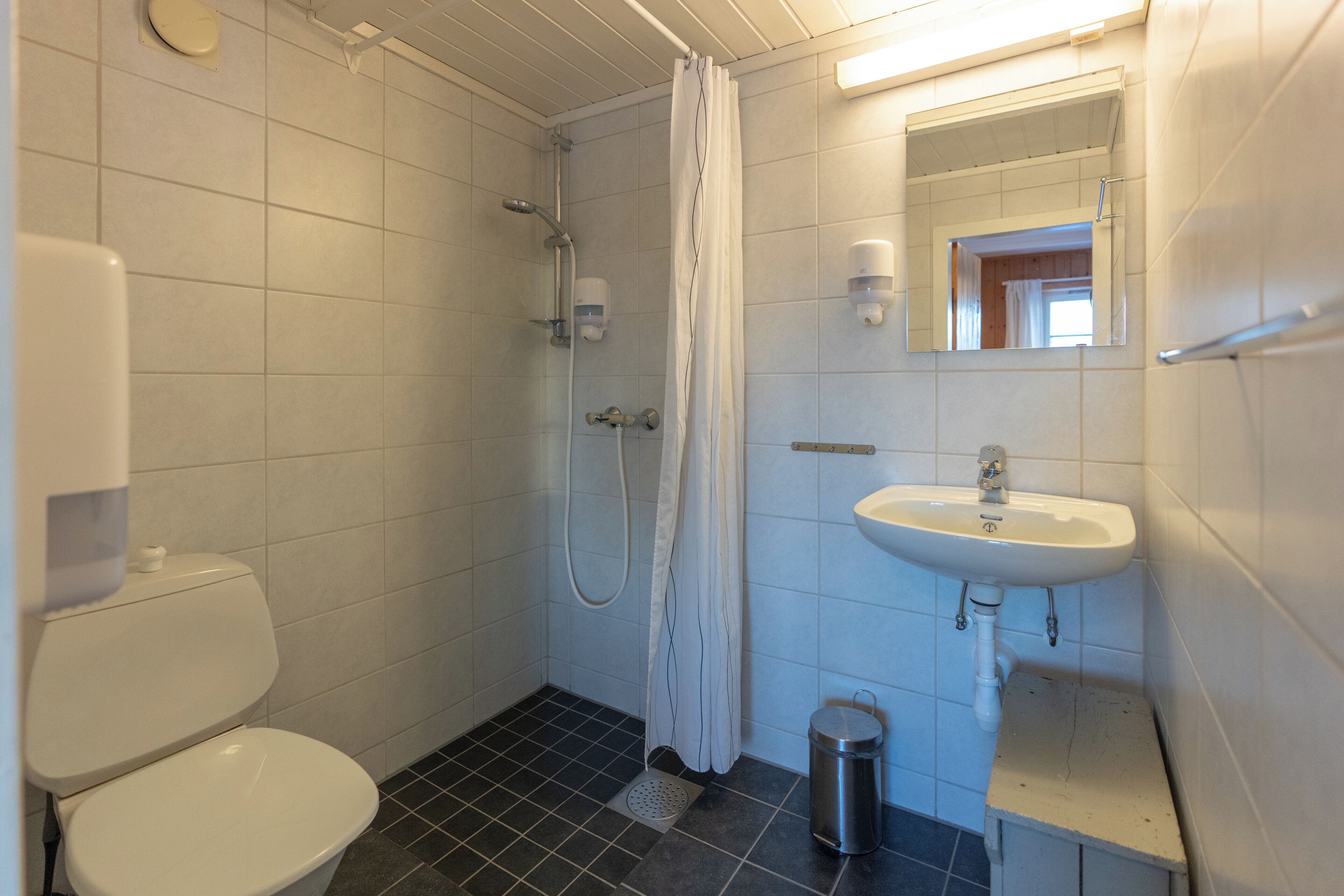 A bathroom with a toilet, shower, sink, and a trash bin.