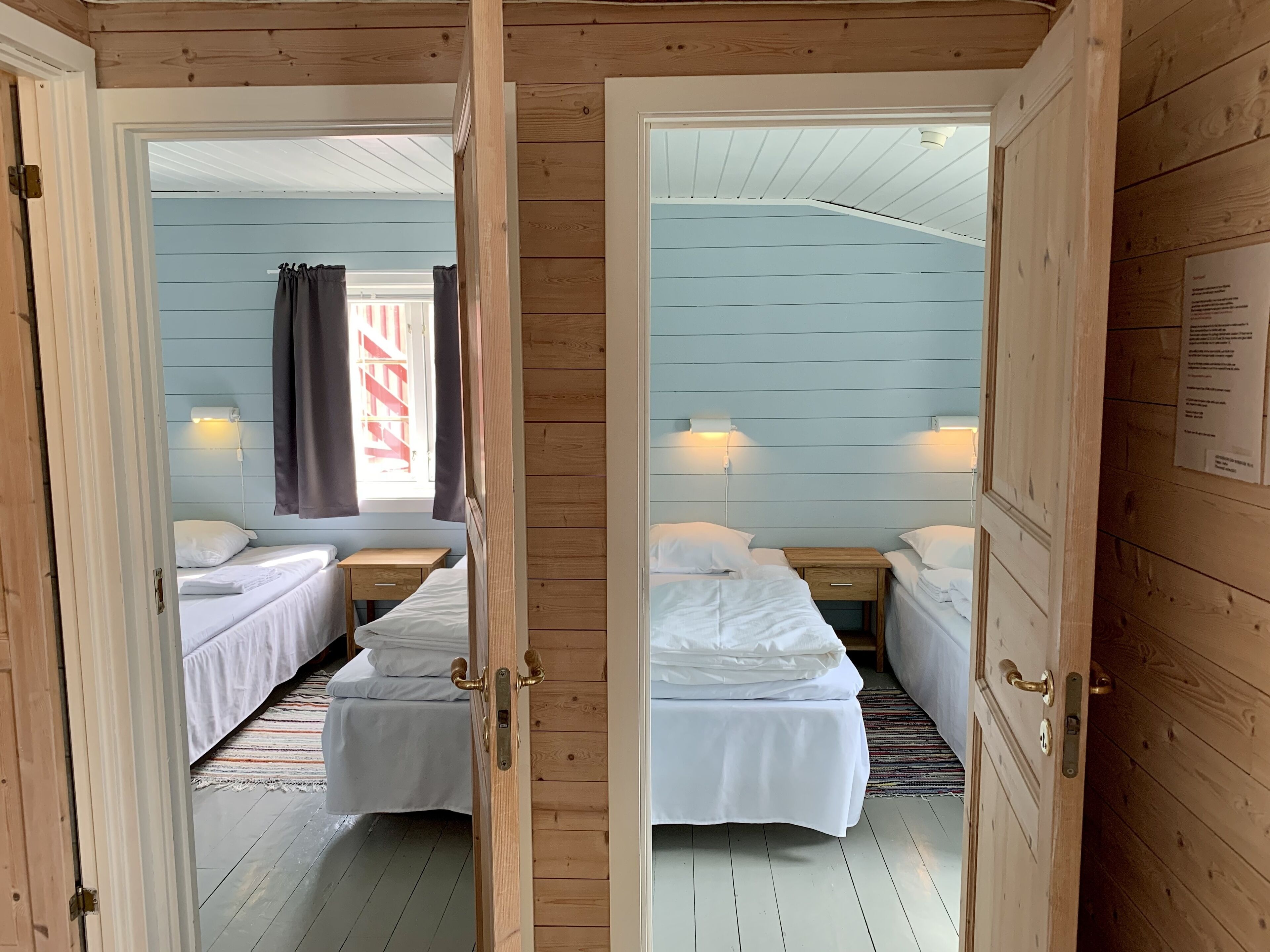 Ein Zimmer mit zwei Betten, Holzwänden und einem Fenster mit Vorhängen.