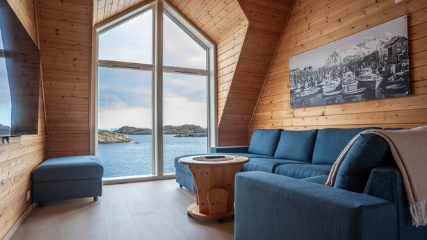 A cozy cabin with a large window offering a view of the water and hills, a blue sofa, and a wooden coffee table.