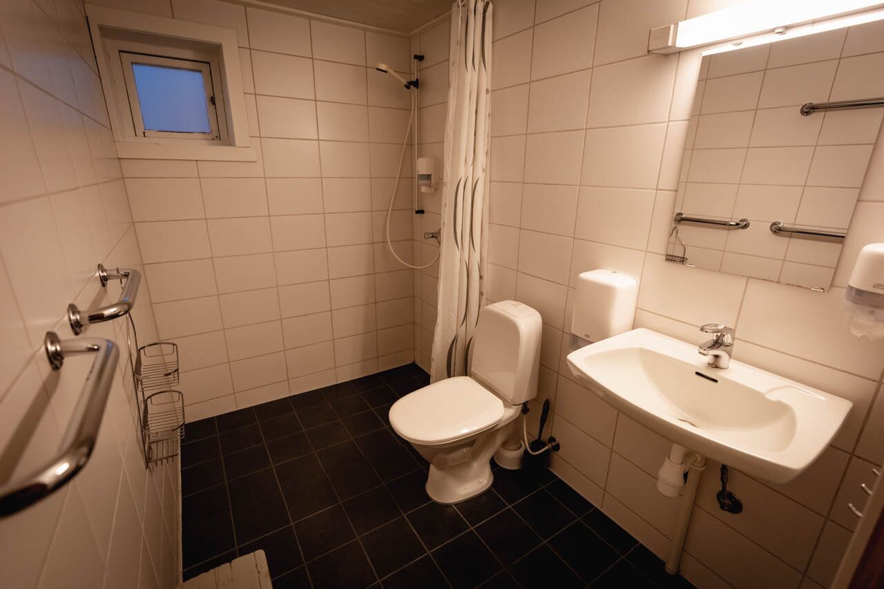 A bathroom with a toilet, sink, shower, and a small window.