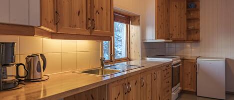 Una cocina con armarios de madera, un lavamanos de acero inoxidable, una tetera y un refrigerador.
