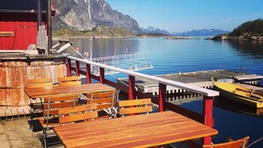 A wooden deck with tables and benches overlooking a calm lake, with mountains in the background.
