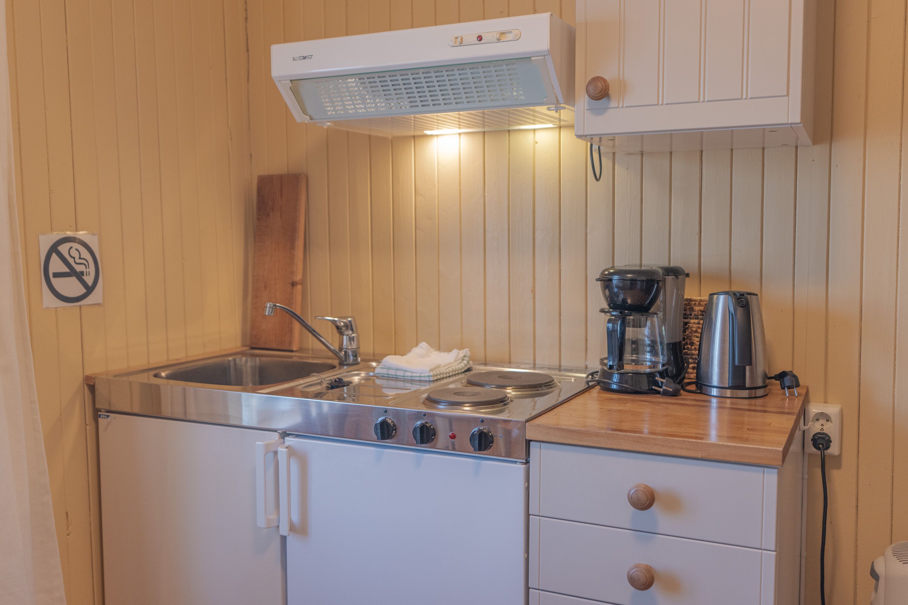 Une cuisine de taille réduite, dotée d’un évier en acier inoxydable, d’une cuisinière et d’une machine à café.
