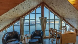 A cozy room with a wooden ceiling, large windows, a dining table, and two leather chairs.