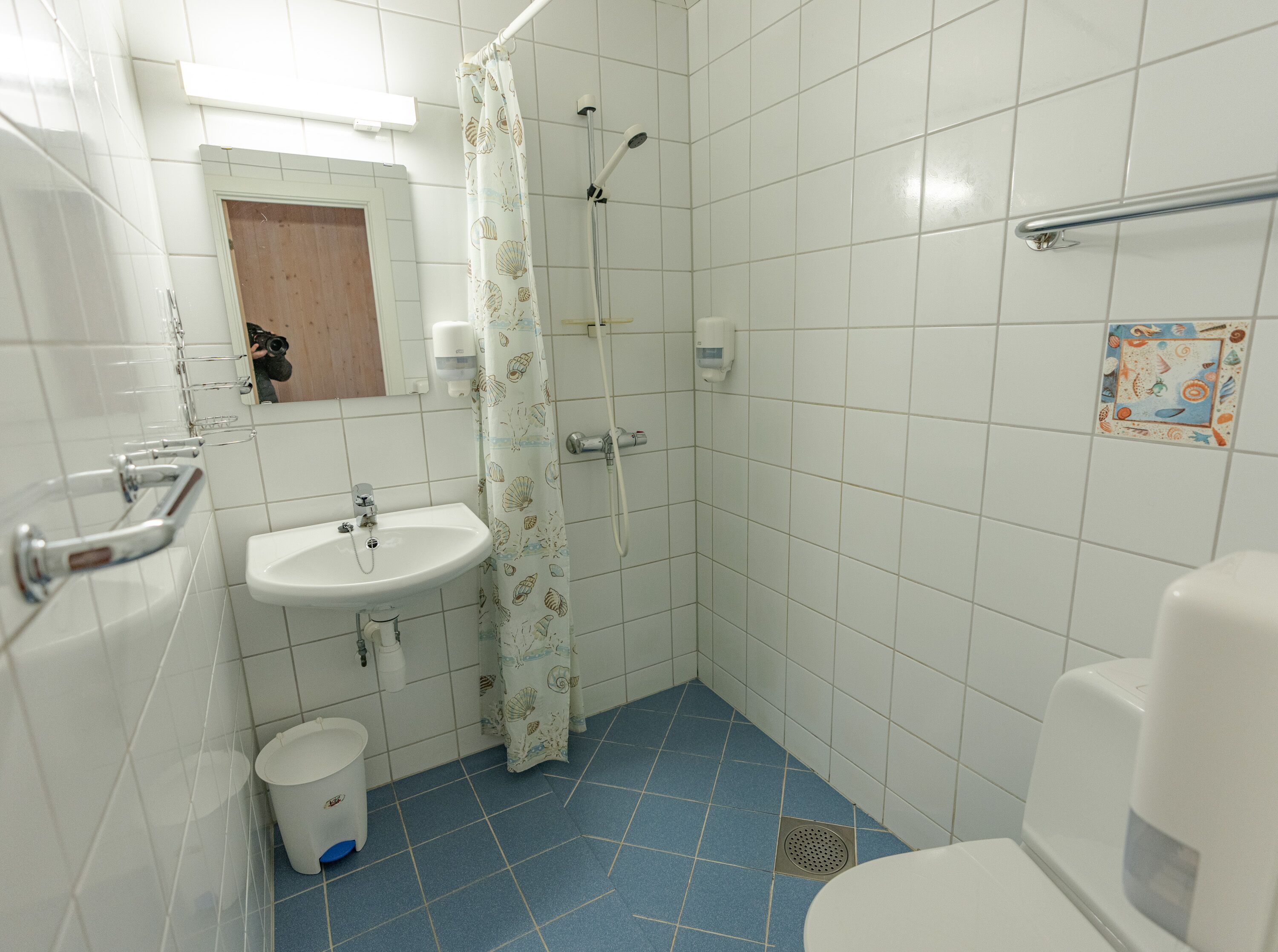 A small bathroom with a sink, toilet, shower, and a blue-tiled floor.