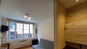 Une pièce avec un mur en bois, un canapé gris, une table à manger avec des chaises et une fenêtre avec des stores.