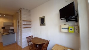 Une cuisine de taille réduite, avec une table et des chaises en bois, un téléviseur fixé au mur et des prises électriques.