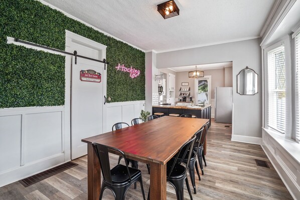 A dining area with a wooden table and black chairs, a neon sign, and a green wall. - *BRAND NEW* The Frances Rose | Hocking Hills Luxury | Family Friendly! (Logan)