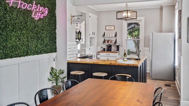 Een moderne keuken met een neonbord, witte kasten en een houten eiland.