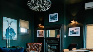 A dark-themed living room with a blue sofa, a leather armchair, a chandelier, and a fireplace.