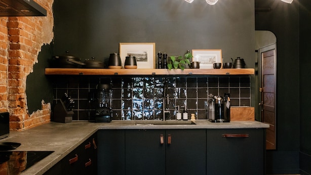 A kitchen with dark cabinetry, a wooden countertop, a black backsplash, and a red patterned rug.