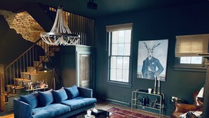 A living room with a blue sofa, a coffee table, a chandelier, a large window, and a rug.