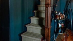 A staircase with wooden steps and a carpeted landing, leading to a room with a brick wall and a wooden door.