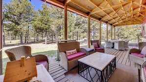 An outdoor covered patio with wicker furniture, a wooden table, and a view of a forest. - 13 Mi to USAFA: Peaceful Colorado Springs Getaway! (Colorado Springs)