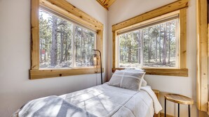 A bedroom with a bed, a nightstand, and a window with a view of a forest. - 13 Mi to USAFA: Peaceful Colorado Springs Getaway! (Colorado Springs)