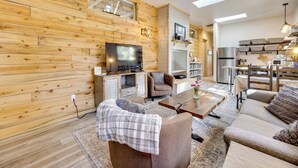 A modern living room with wooden walls, a flat-screen TV, a sofa, a coffee table, and a dining area with a kitchen in the background. - 13 Mi to USAFA: Peaceful Colorado Springs Getaway! (Colorado Springs)