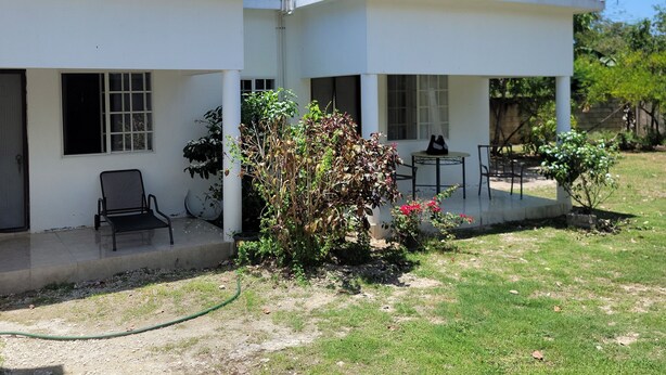 Um edifício de dois andares com telhado plano e grandes janelas. Possui área externa coberta com cadeiras e uma mesa.
