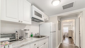 A kitchen with white cabinets, a microwave, a toaster, a sink, and a refrigerator. - The Roosevelt Suite (2 BEDROOMS/2 BATHS) (Stuart)