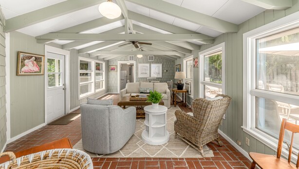 A spacious sunroom with a high ceiling, large windows, and a variety of seating options including a sofa, chairs, and a wicker chair. - The Roosevelt Suite (2 BEDROOMS/2 BATHS) (Stuart)