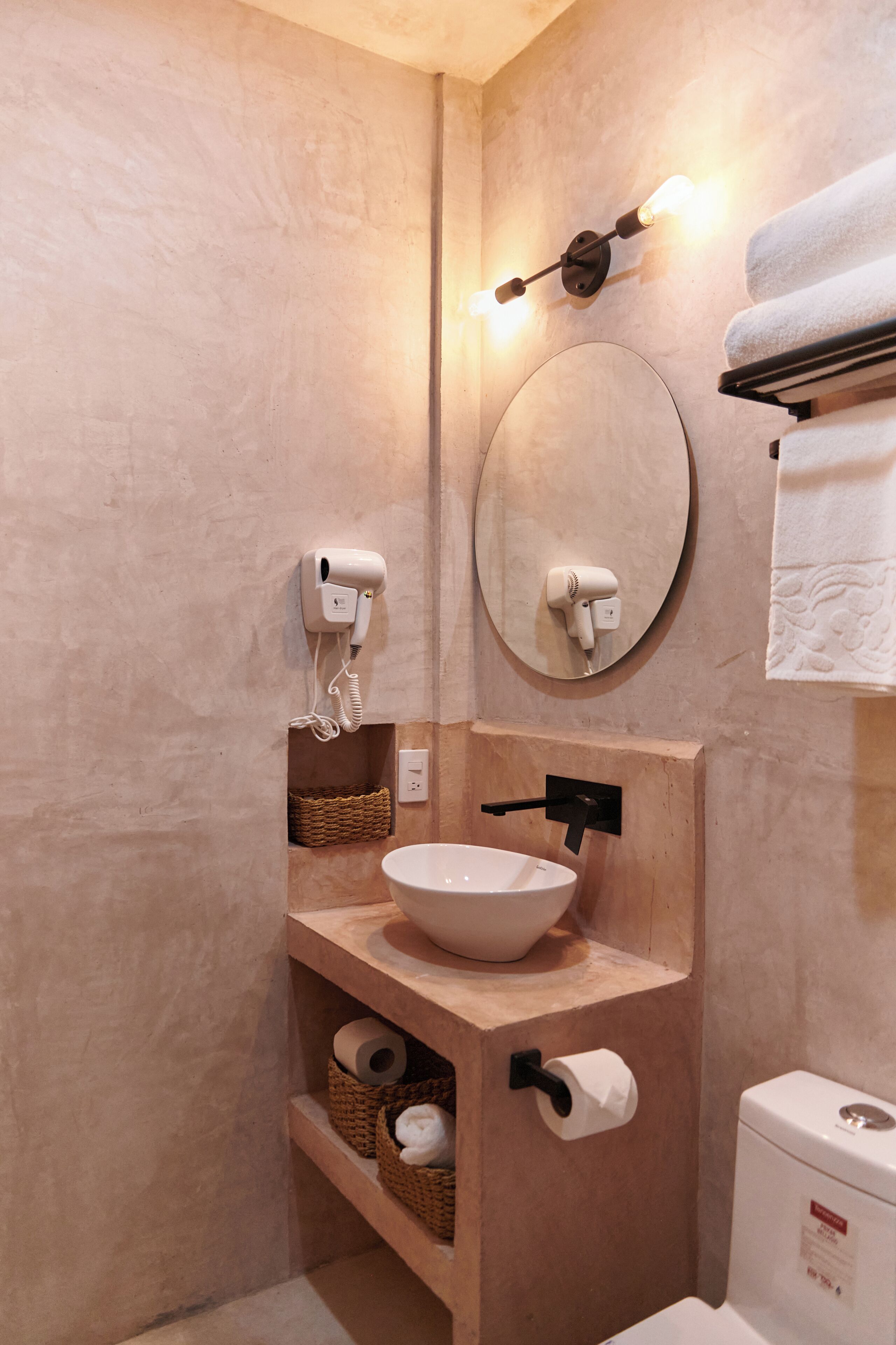 A modern bathroom with a wooden vanity, a round mirror, a towel rack, and a toilet.