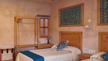 A room with two beds, a ceiling fan, a wooden wardrobe, and patterned wall hangings.