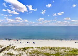 A beach with clear skies, calm water, and a sandy shore with umbrellas and beach chairs. - On The Beach! Summer 2026 dates still available. (Gulf Shores)