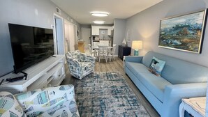 Uma sala de estar moderna com uma televisão de tela plana, um banquinho estampado, um sofá azul claro e um quadro na parede.