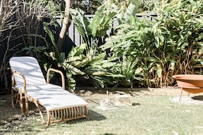 Relax in the serene garden, surrounded by lush plants and a comfortable wicker lounge chair.