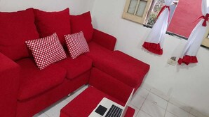 A red sofa with two patterned pillows, a small white table, and a window with red curtains. - 5 minutes from the airport, the comercial city, is a place will be in pace, save (Luque)