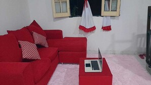 A red sofa with patterned pillows, a laptop on a matching ottoman, and a window with curtains. - 5 minutes from the airport, the comercial city, is a place will be in pace, save (Luque)
