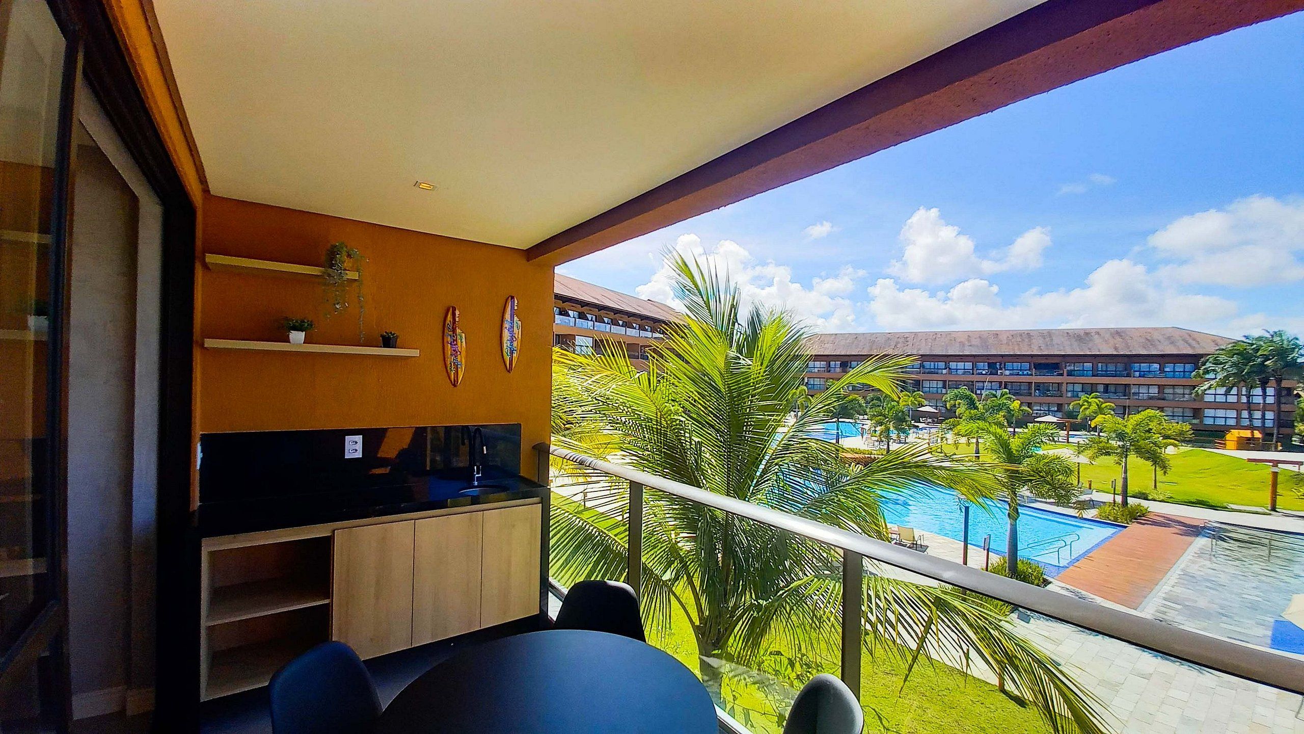 Un balcón con vista a una piscina, un edificio al fondo y una planta en la pared.