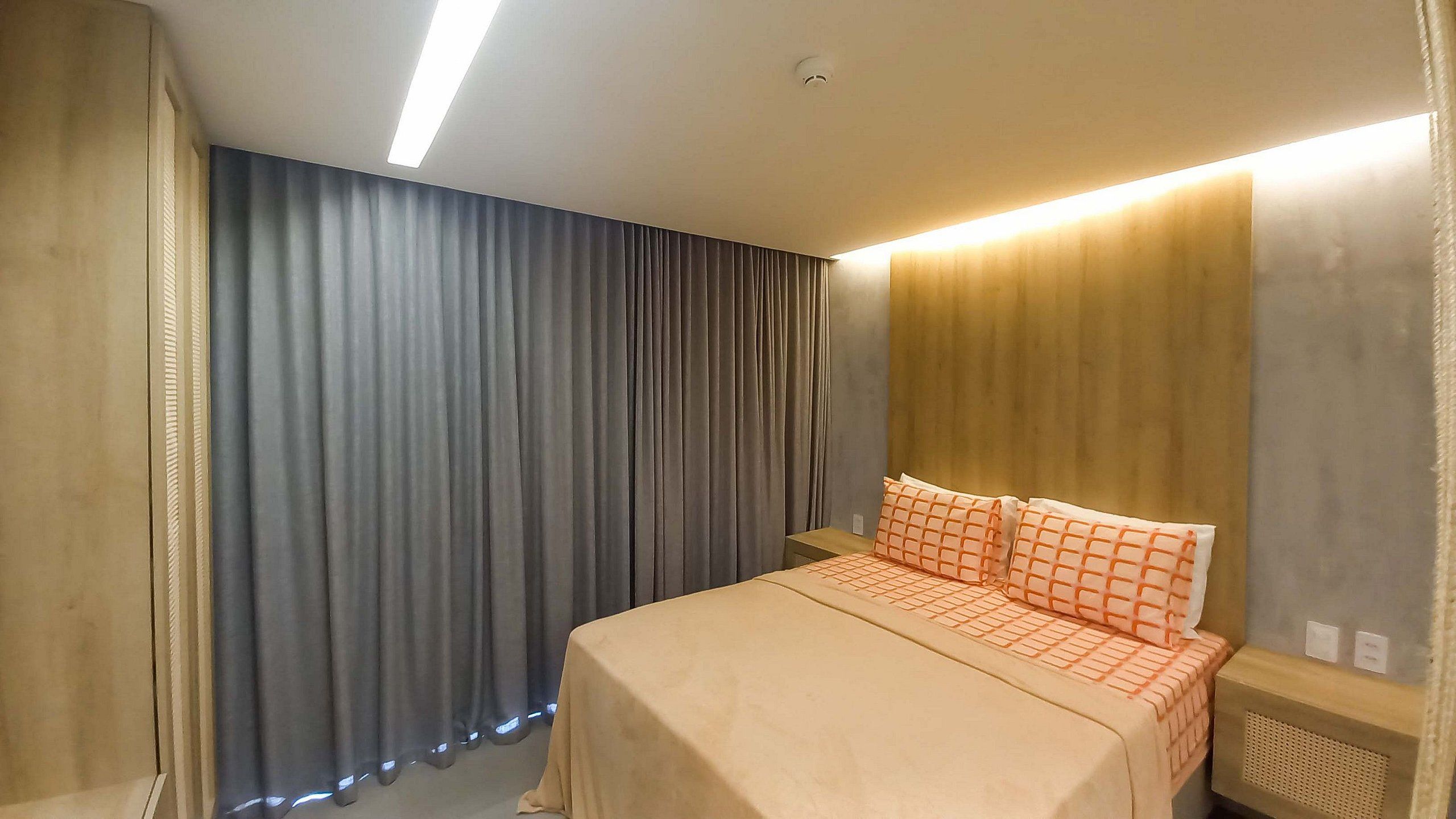 A hotel room with a bed, curtains, and a headboard with built-in lighting.