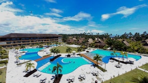 A resort with multiple swimming pools, palm trees, and a large building in the background.