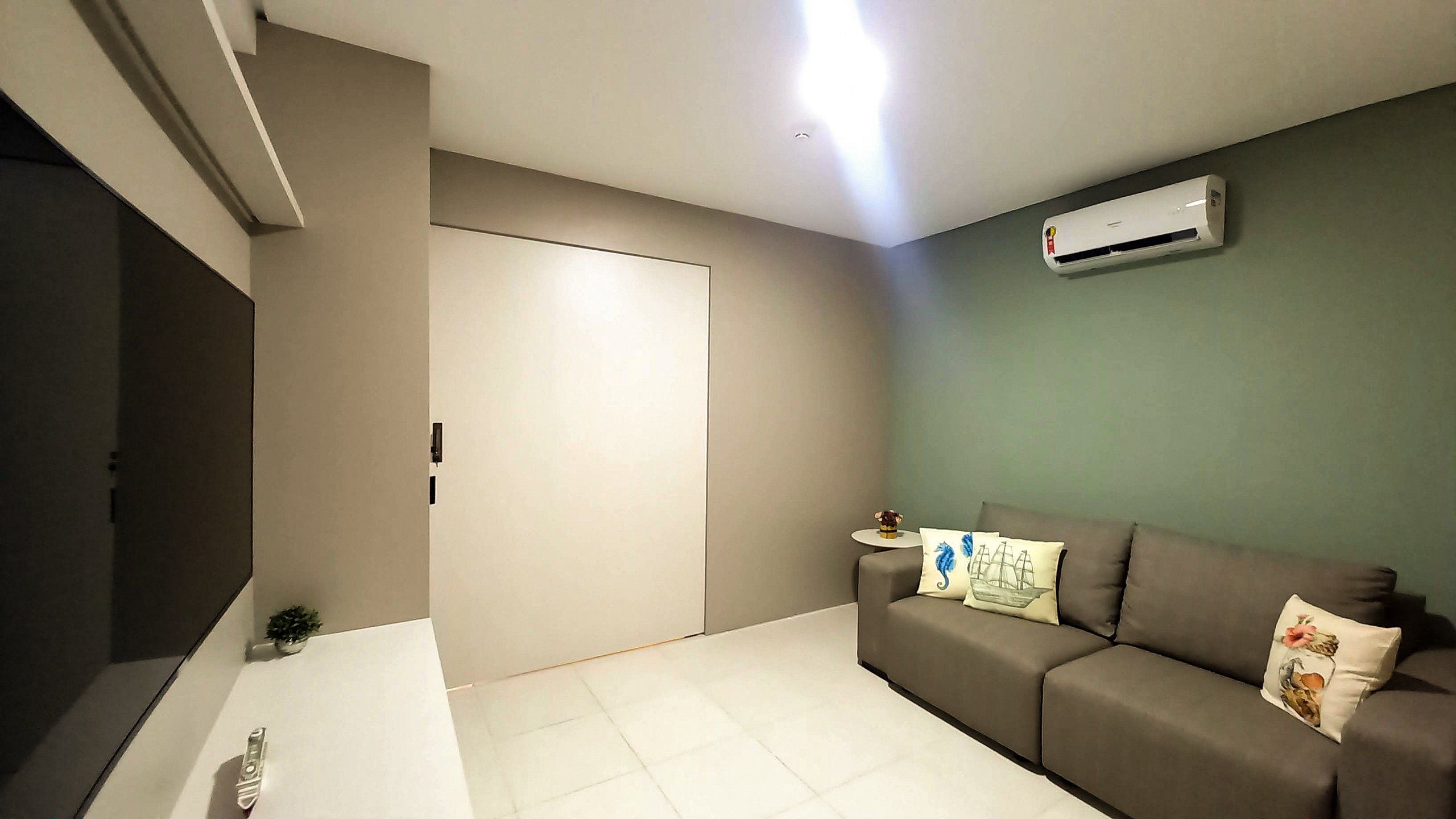 A living room with a sofa, a small table with a vase, and an air conditioning unit on the wall.