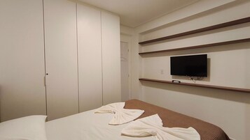 Un dormitorio con una cama, un televisor en un estante y un armario.