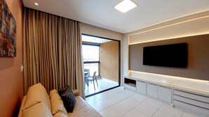 Un salon moderne avec un canapé, un téléviseur et une vue sur l’extérieur.