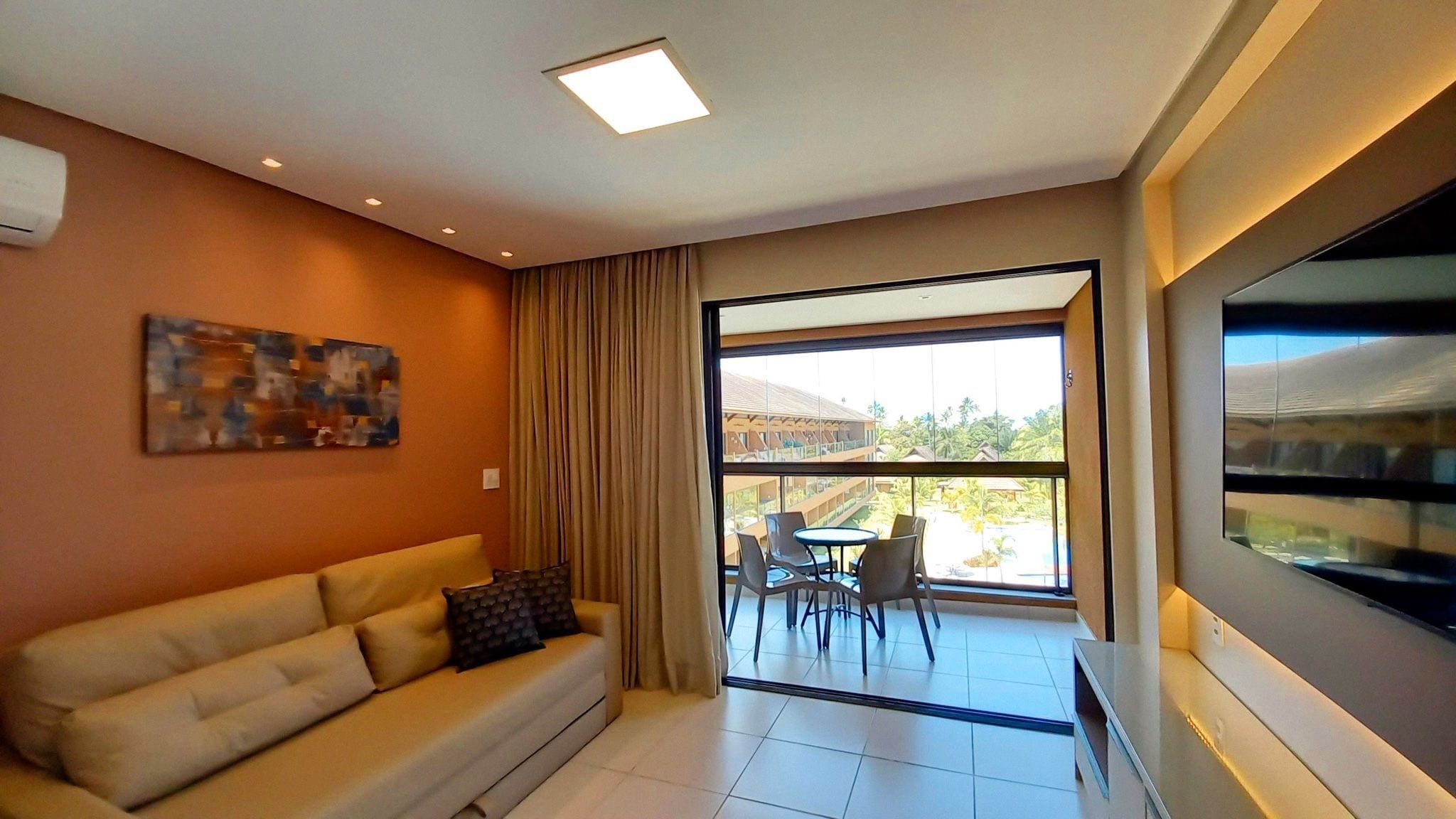 A modern living room with a sofa, a painting, a dining area with chairs, and a large window offering a view.