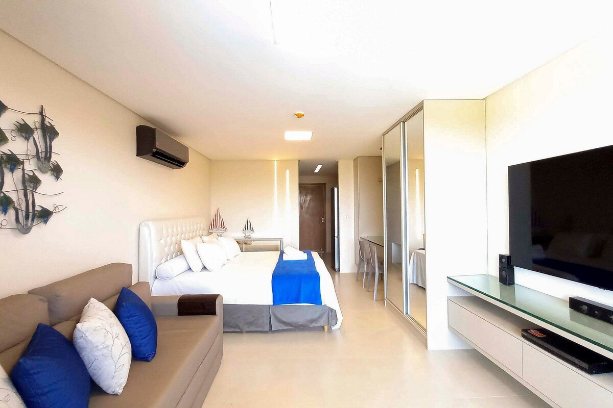 A hotel room with a bed, a sofa, a TV, and a wall-mounted artwork.