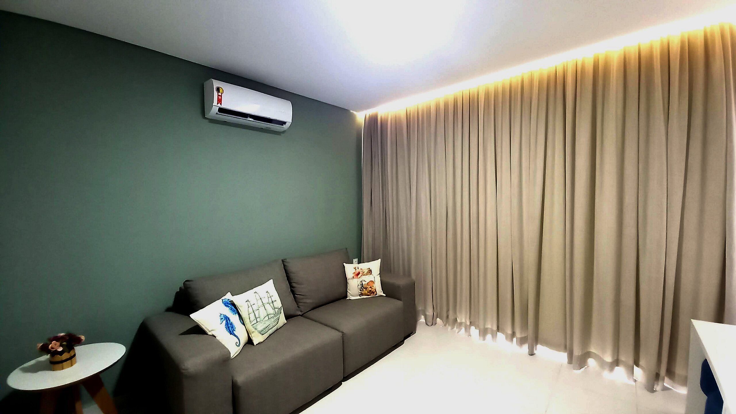 A modern living room with a grey sofa, a small round table, and a wall-mounted air conditioner.