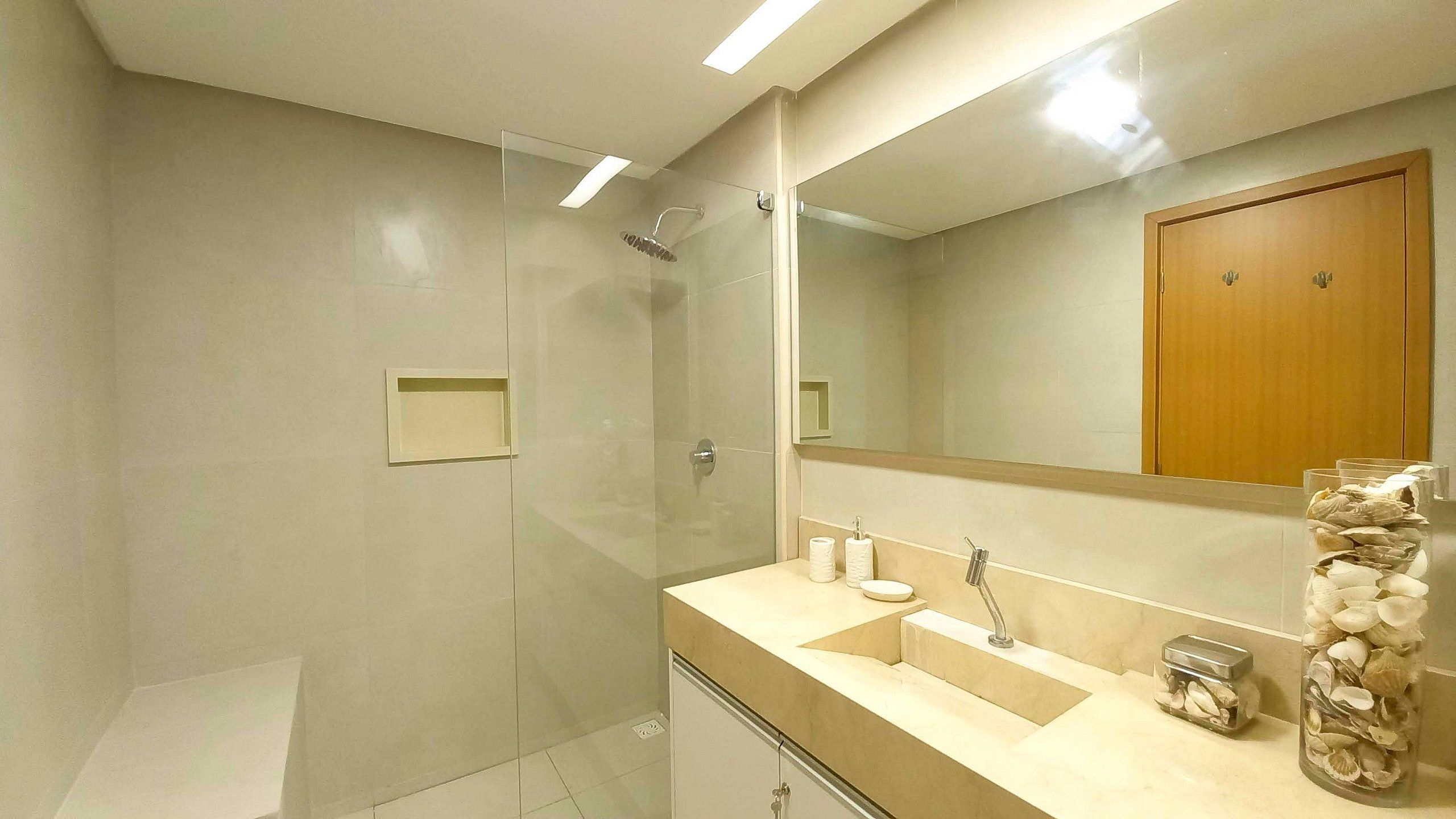 A modern bathroom with a glass shower enclosure, a vanity with a sink and mirror, and a decorative jar of seashells.