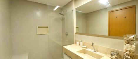 A modern bathroom with a glass shower enclosure, a vanity with a sink and mirror, and a decorative jar of seashells.
