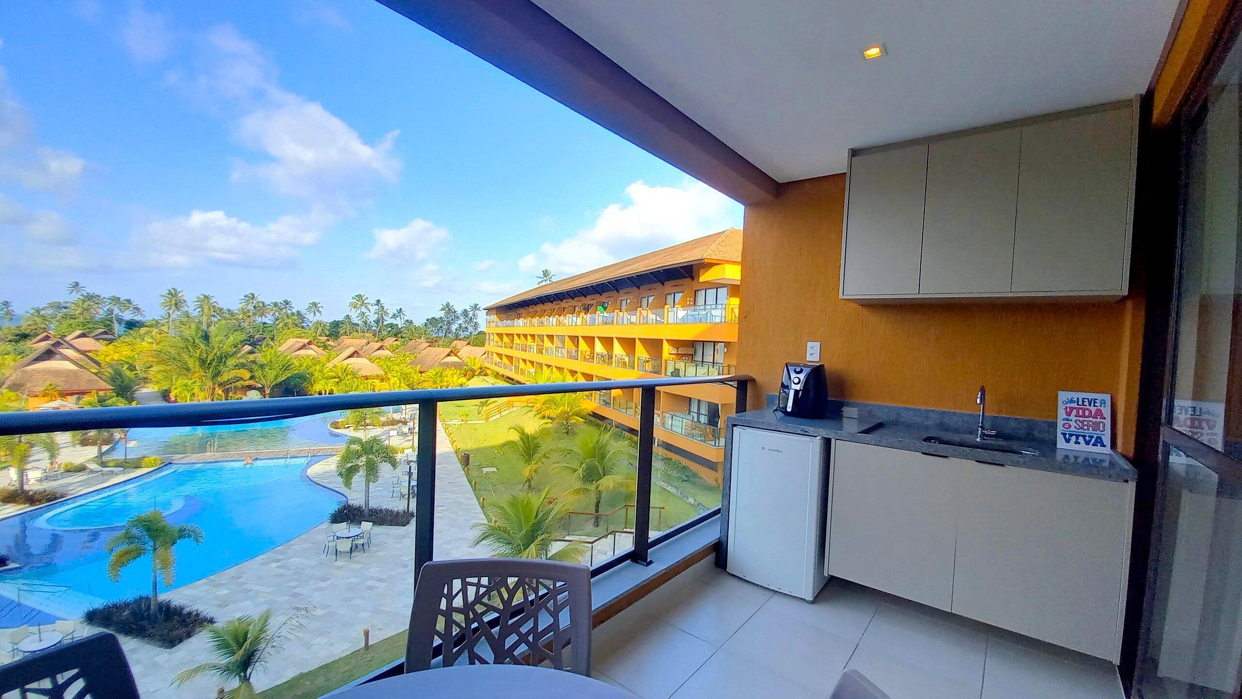 A balcony with a view of a swimming pool, a kitchen area, and a building with multiple balconies.