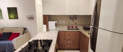 A compact kitchen with a gas stove, wooden cabinets, a refrigerator, and a countertop.