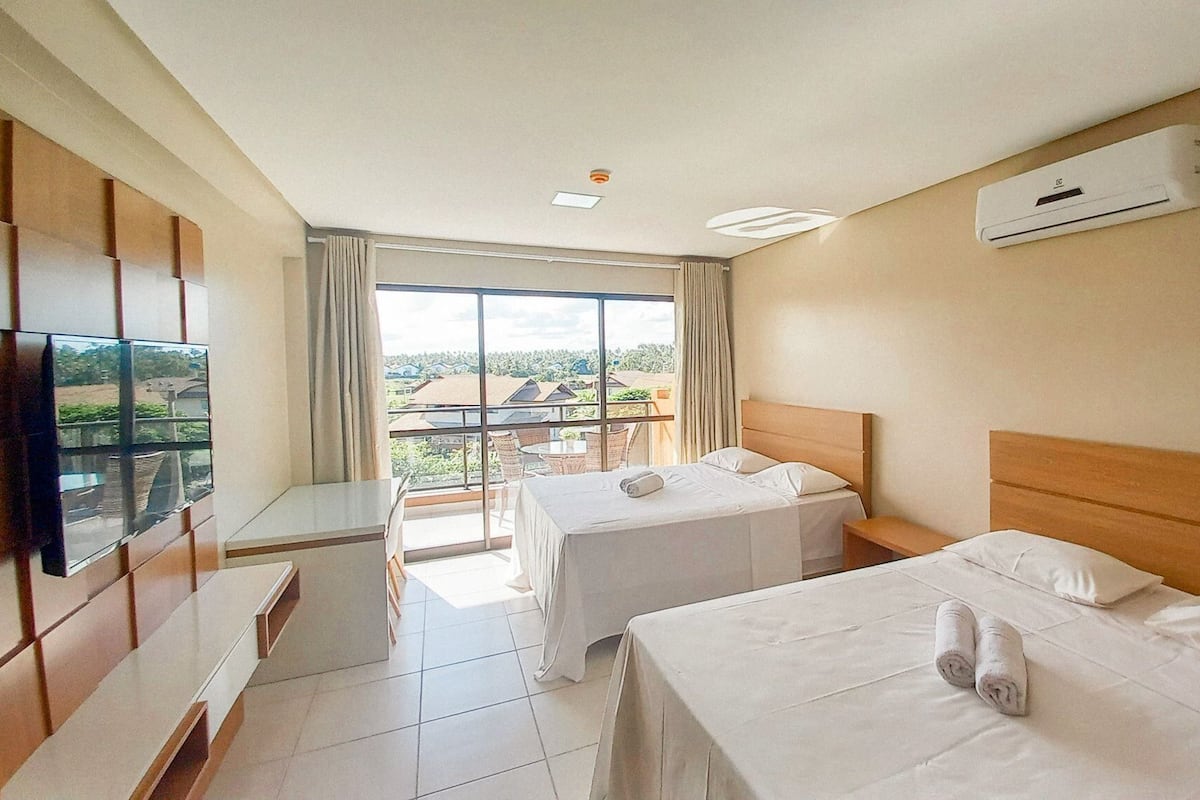 A hotel room with two beds, a TV, a balcony with a view, and an air conditioning unit.