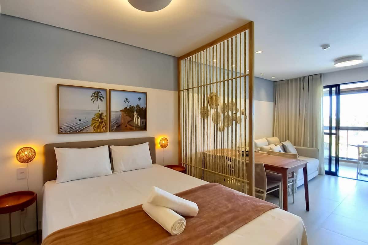 A hotel room with a bed, a desk, a chair, and a large window.