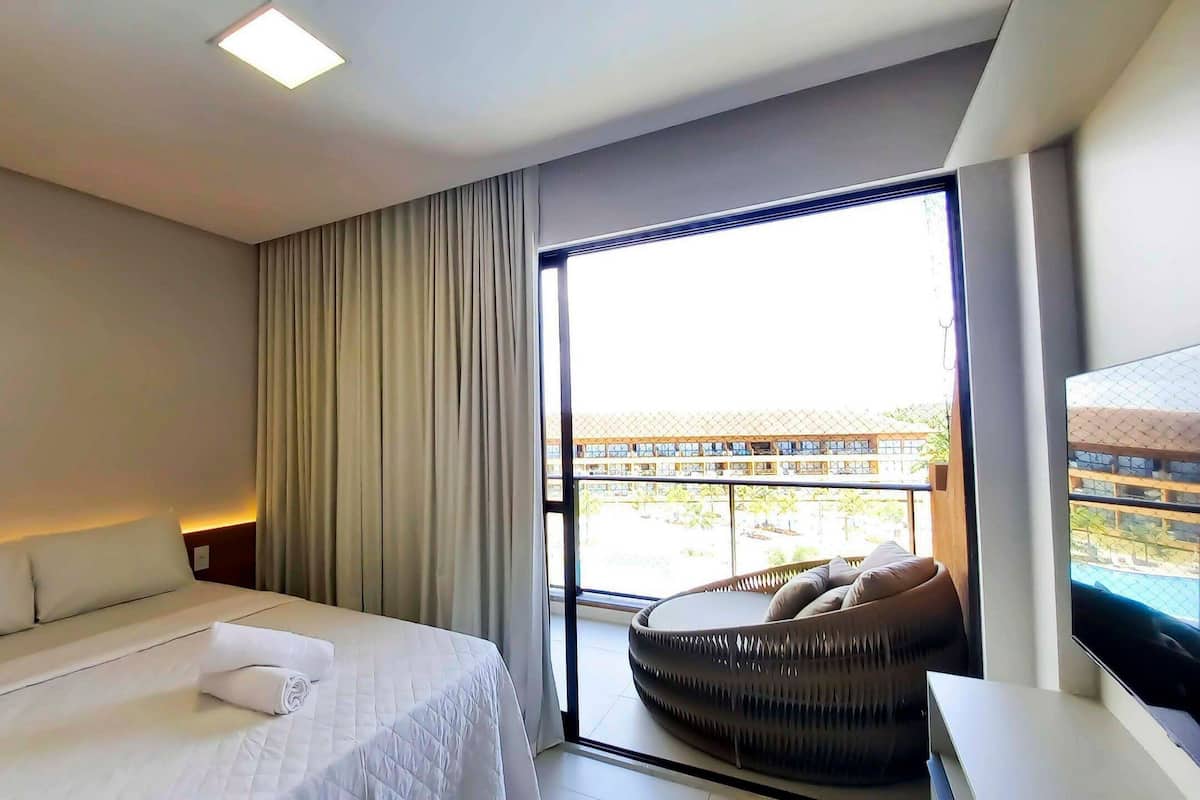 A hotel room with a bed, a large window, a balcony, and a seating area.