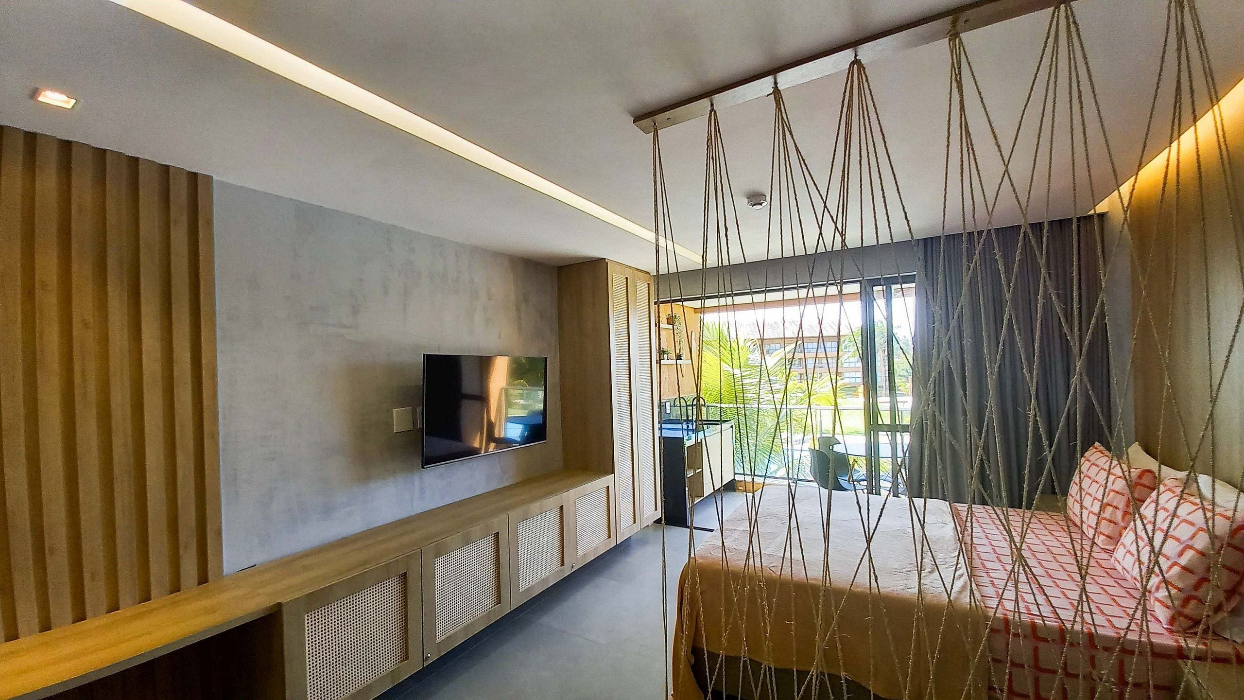 Une chambre d’hôtel moderne équipée d’une télévision, d’un lit, d’un fauteuil suspendu et offrant une vue sur l’extérieur.