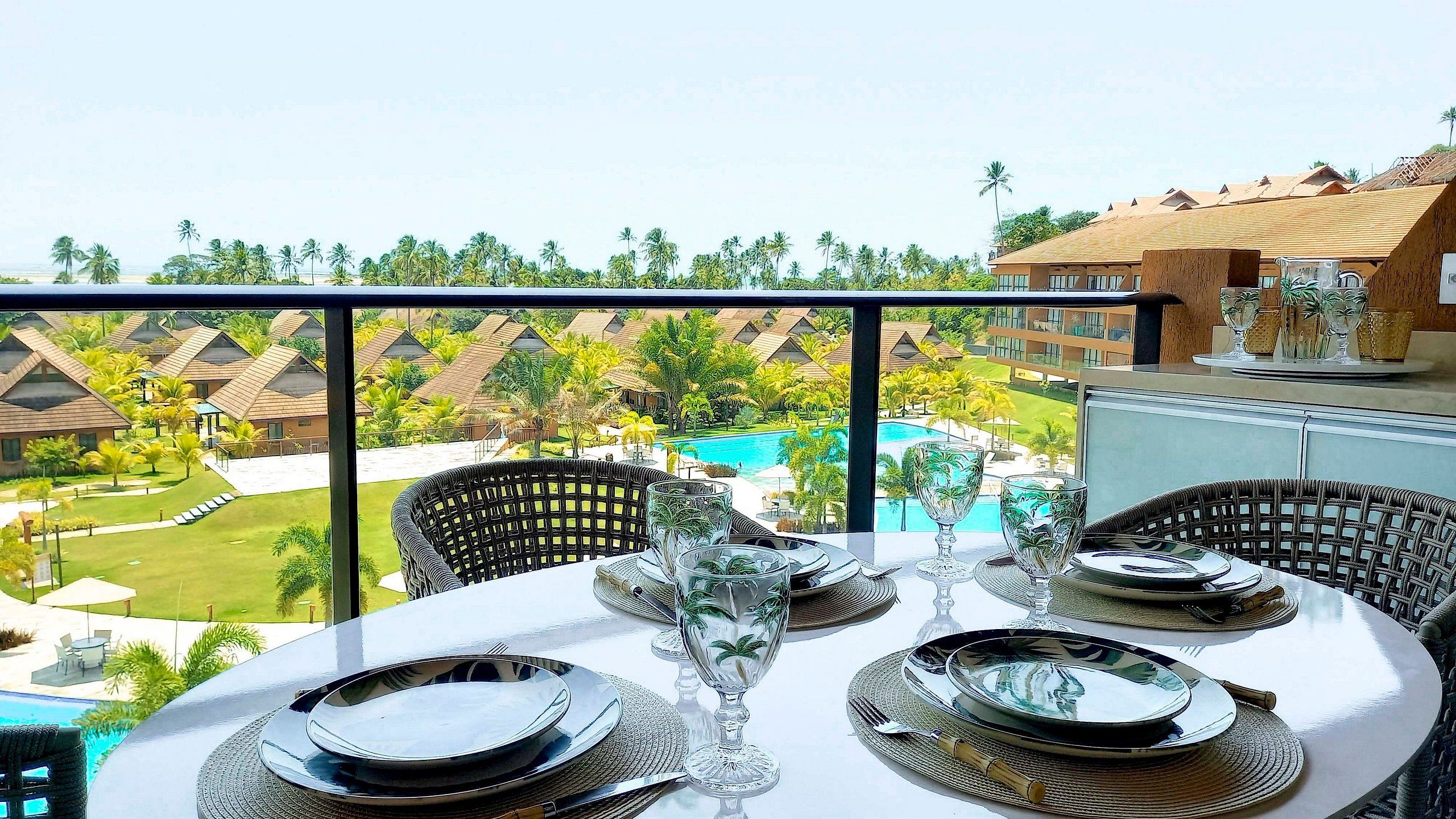 A dining area with a table set for four, overlooking a pool and resort buildings.