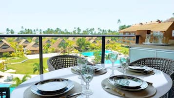 A dining area with a table set for four, overlooking a pool and resort buildings.